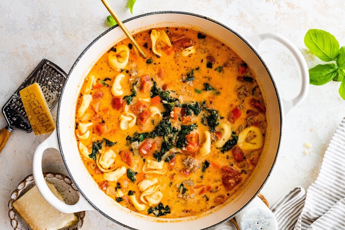 creamy Italian sausage tortellini soup in pot with ladle.