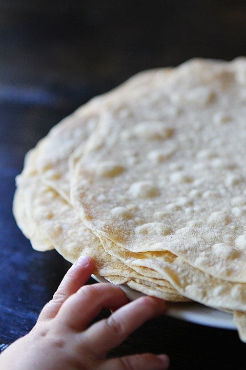 Homemade Flour Tortillas Recipe on twopeasandtheirpod.com Make fresh tortillas at home! You will never buy them again! small hand reaching for plate of homemade flour tortillas