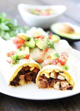 Breakfast burrito on plate topped with avocado and tomato