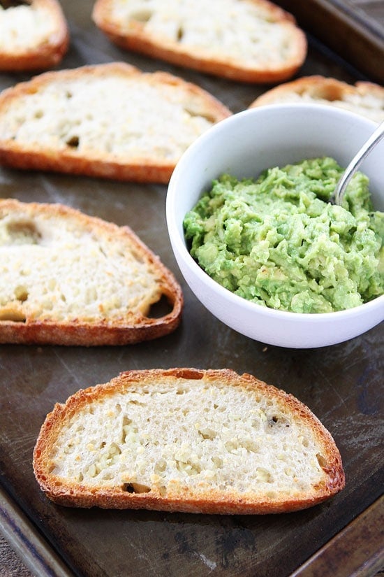Garlic Bread Avocado Toasts Recipe on twopeasandtheirpod.com The avocado takes this garlic bread to a whole new level! Spooning avocado mash for Garlic Avocado Toast Recipe