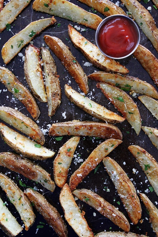Baked Garlic Parmesan Potato Wedges Recipe on twopeasandtheirpod.com These easy baked oven fries are our favorite! They are great with any meal! baked potato wedges with ketchup on baking sheet