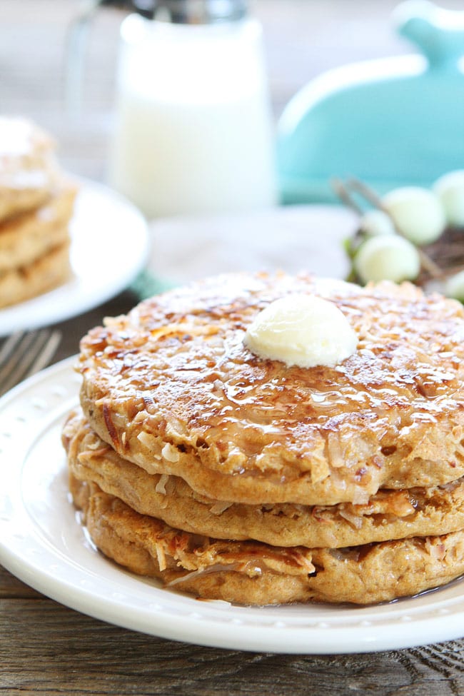 Toasted Coconut Pancakes Recipe on twopeasandtheirpod.com Light and fluffy pancakes with a sweet toasted coconut topping! These pancakes are perfection! Melted butter on stack of Coconut milk Pancakes