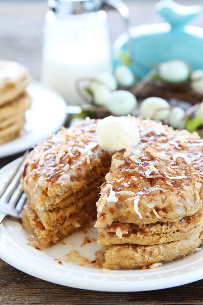 Toasted Coconut Pancakes Recipe on twopeasandtheirpod.com Light and fluffy pancakes with a sweet toasted coconut topping! These pancakes are perfect for Easter brunch! Plate of stacked Toasted Coconut Pancakes with butter