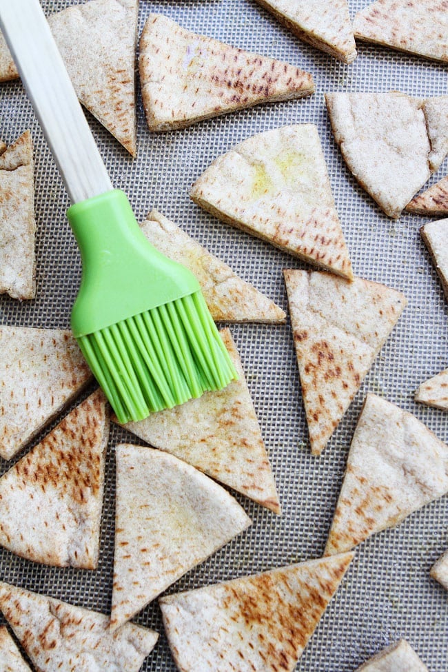 Homemade Pita Chips Recipe on twopeasandtheirpod.com How to make your own pita chips at home! They are so easy and so good! pita chips being brushed with olive oil on baking sheet.