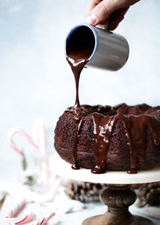 Chocolate Peppermint Bundt Cake Recipe on twopeasandtheirpod.com Moist chocolate sour cream bundt cake drizzled with a silky smooth chocolate glaze and garnished with crushed peppermint candies. This cake is the perfect holiday dessert! Chocolate glaze being poured over Chocolate Peppermint Bundt Cake on cake stand.