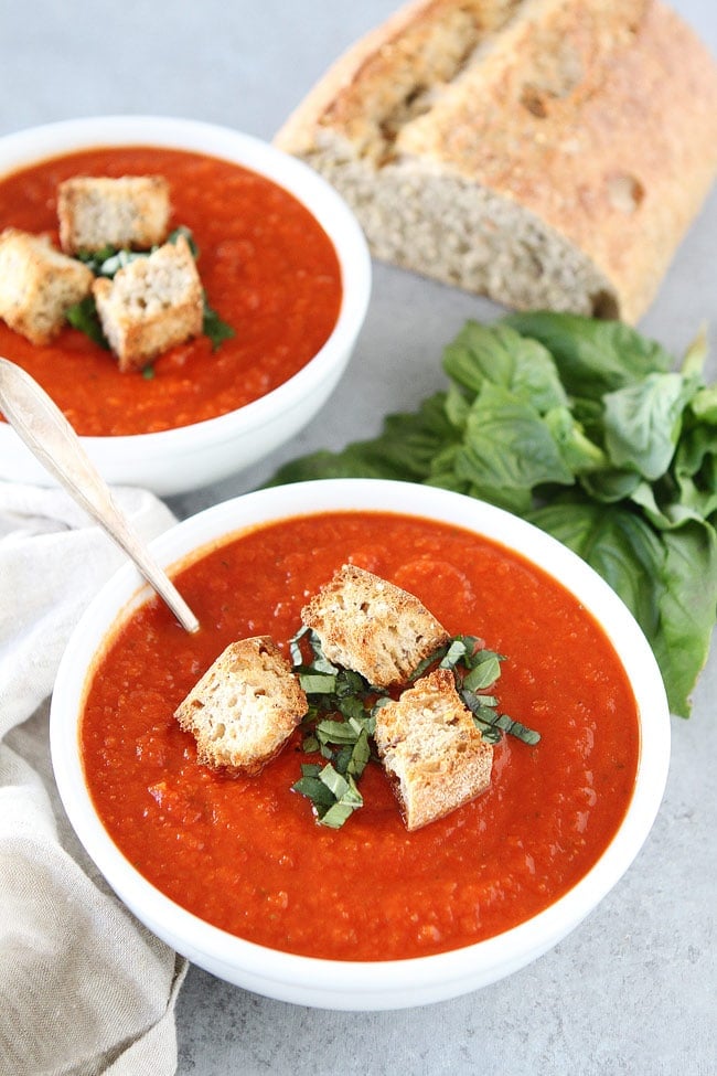 Roasted Red Pepper Tomato Soup Recipe on twopeasandtheirpod.com This simple and satisfying tomato soup is made with pantry staples and takes less than 30 minutes to make. Roasted Red Pepper Tomato Soup Recipe in white bowls with croutons and basil.