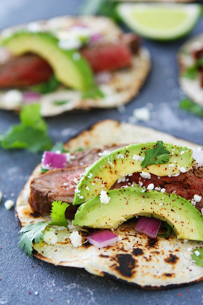 Steak tacos with avocado, cilantro, red onion, and queso fresco.