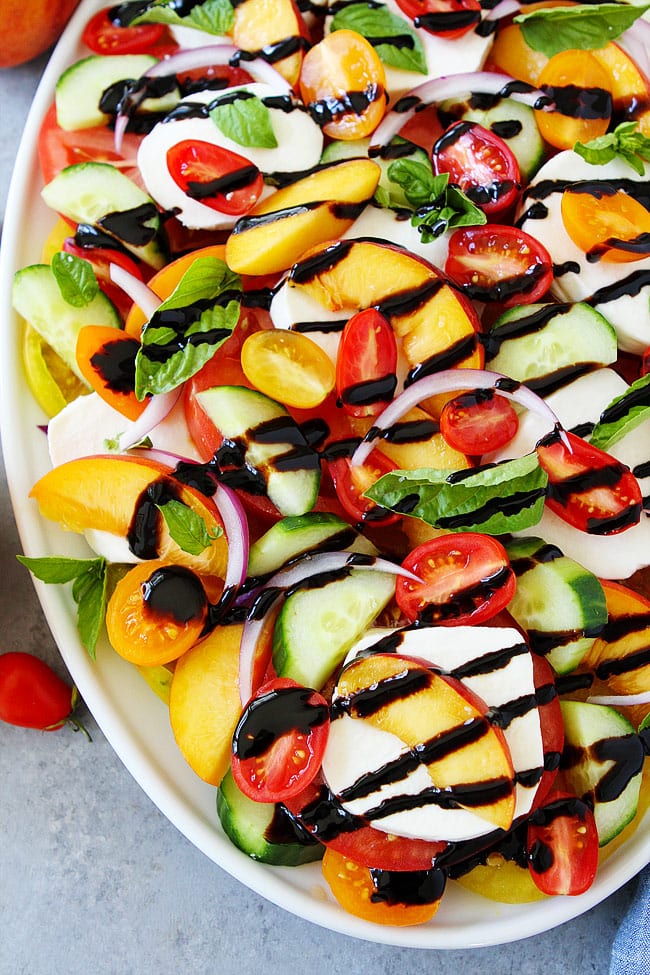 Summer Caprese Salad made with tomatoes, peaches, cucumber, fresh mozzarella cheese, red onion, basil, and a simple balsamic glaze. This easy summer salad takes minutes to make. Colorful Caprese Salad on platter ready to serve