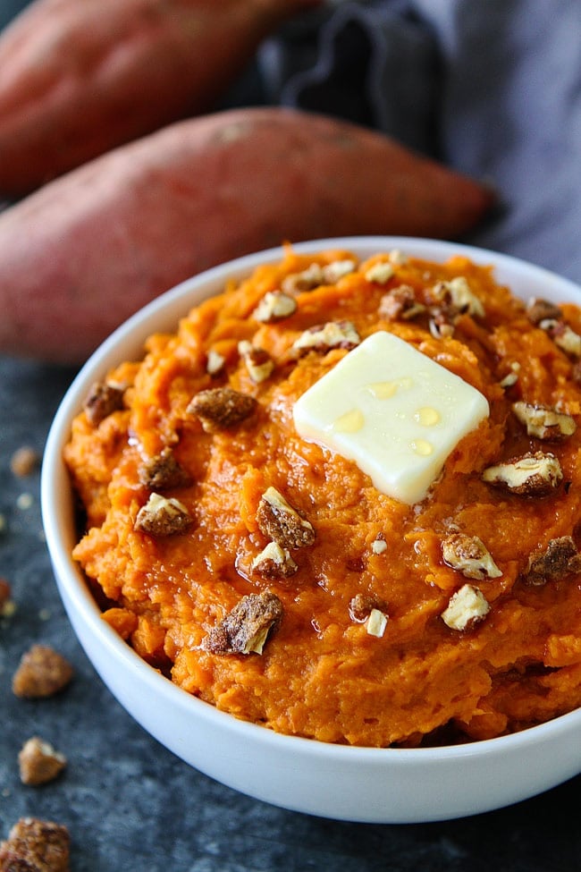 Mashed sweet potatoes in bowl with candied pecans and butter.