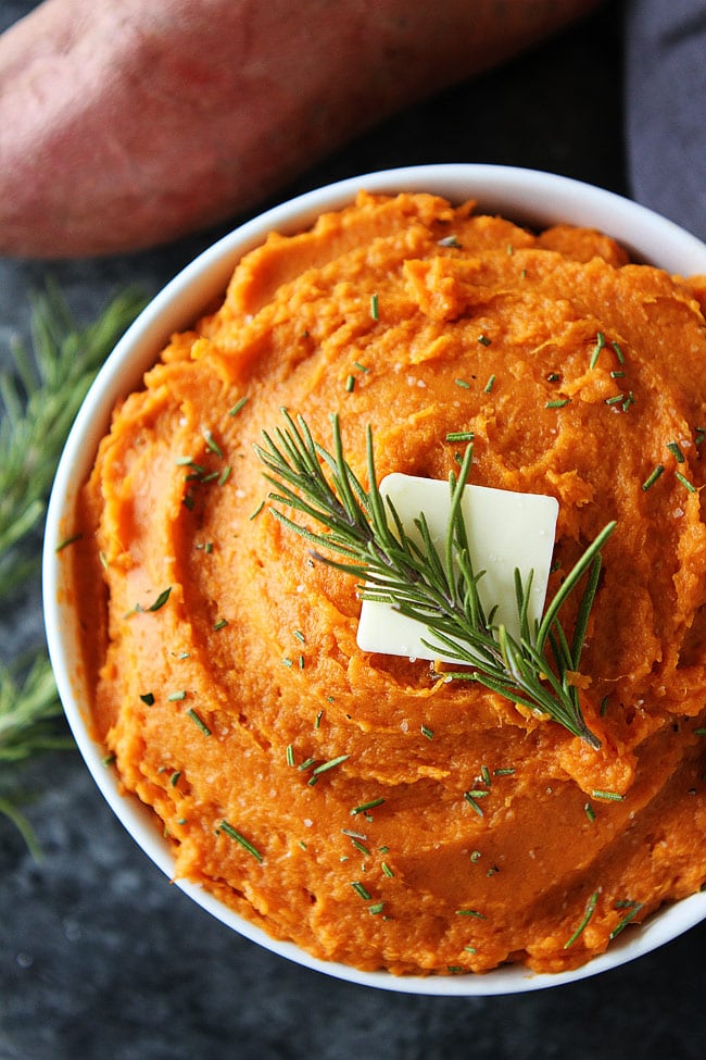 Mashed Sweet Potatoes in bowl with butter and rosemary.