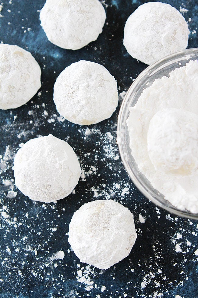 Mexican wedding cookies being rolled in powdered sugar in bowl.