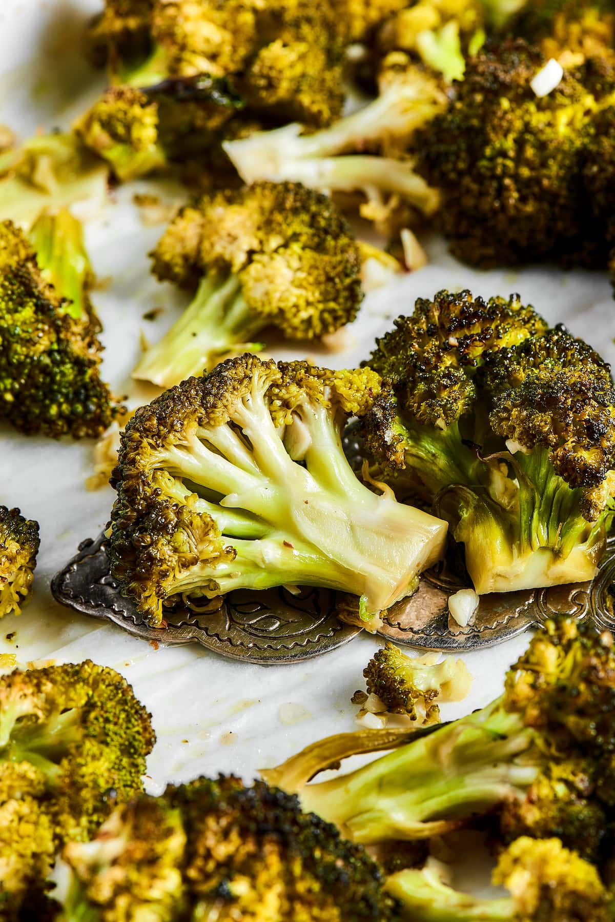 Easy roasted broccoli with garlic is destined to be your new go-to side dish! This crispy, oven-baked broccoli recipe is even kid-approved. Roasted broccoli on white parchment paper.