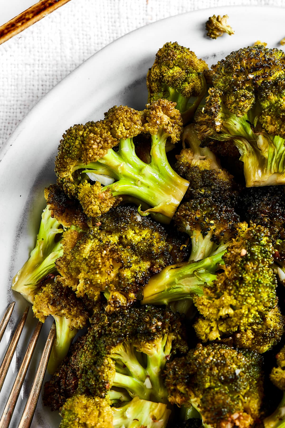 Easy roasted broccoli with garlic is destined to be your new go-to side dish! This crispy, oven-baked broccoli recipe is even kid-approved. Close up of a bowl of roasted broccoli next to a fork.