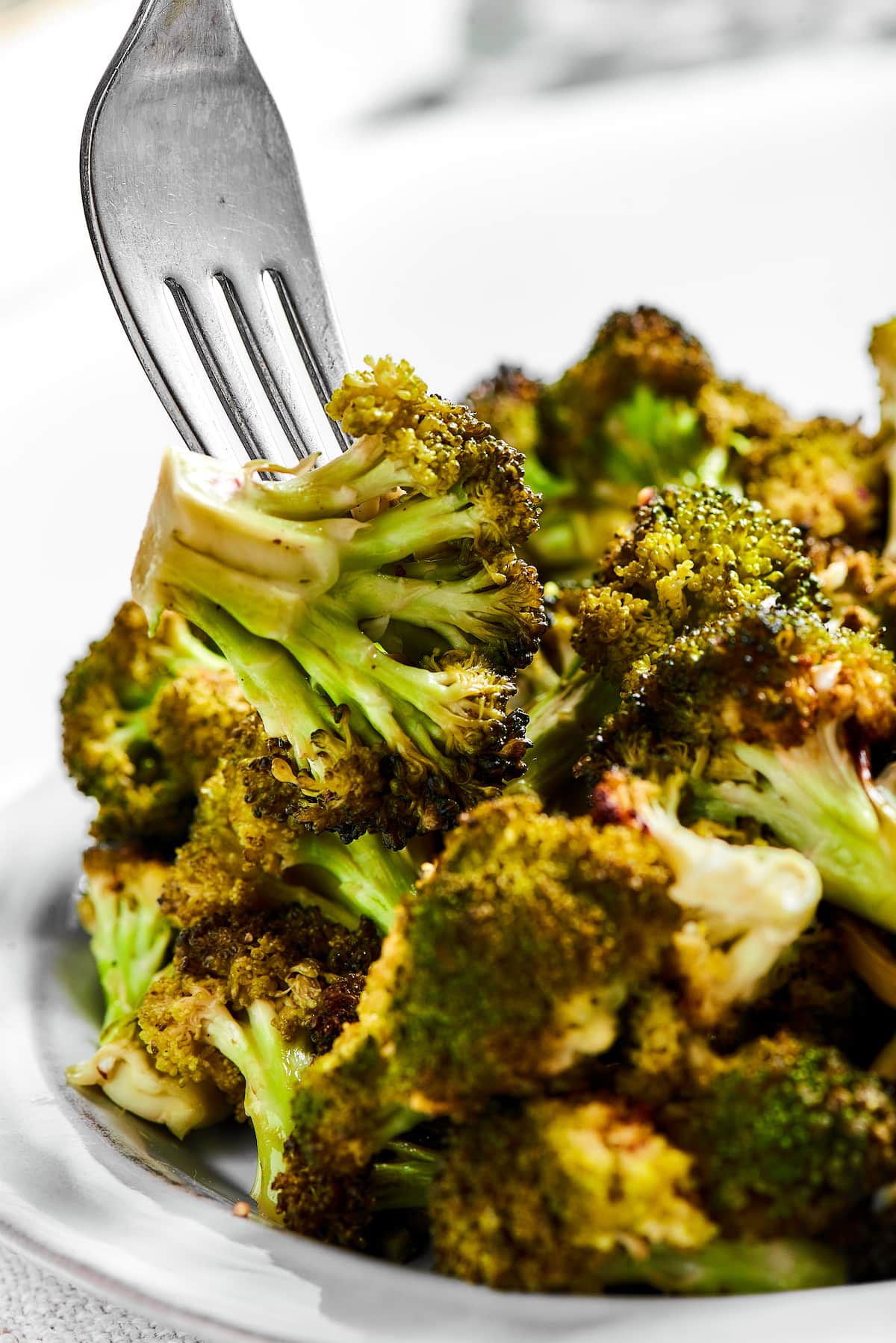Easy roasted broccoli with garlic is destined to be your new go-to side dish! This crispy, oven-baked broccoli recipe is even kid-approved. A fork picks up a broccoli floret from a bowl of roasted broccoli.