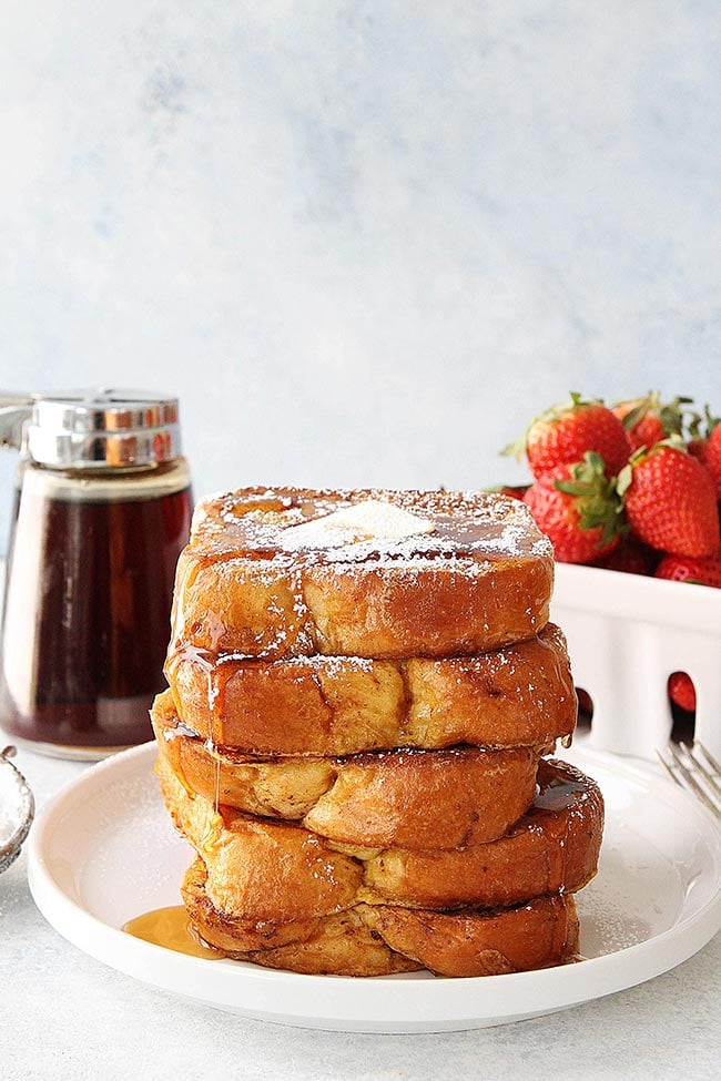 This easy French Toast recipe is a family favorite! Make it for breakfast this weekend! #breakfast #brunch #easyrecipe #frenchtoast large stack of brioche French toast on plate with butter, powdered sugar, and maple syrup.