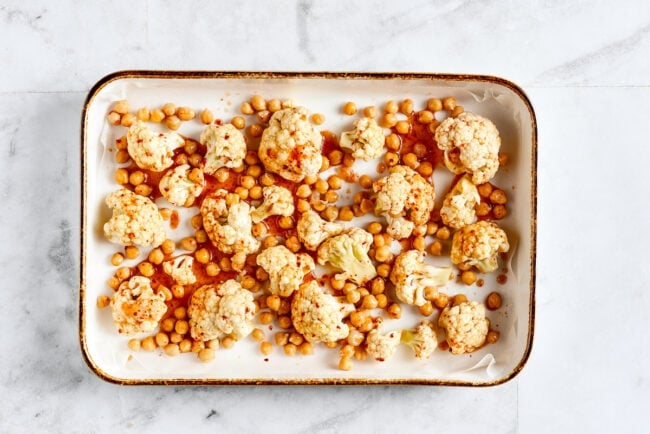 These roasted cauliflower and chickpea tacos are spicy, fresh, bursting with flavor, and a healthy vegetarian Mexican dinner A roasting pan lined with parchment paper and filled with cauliflower and chickpeas that are coated in lime juice, olive oil, chili powder, cumin, onion powder, garlic powder, and salt