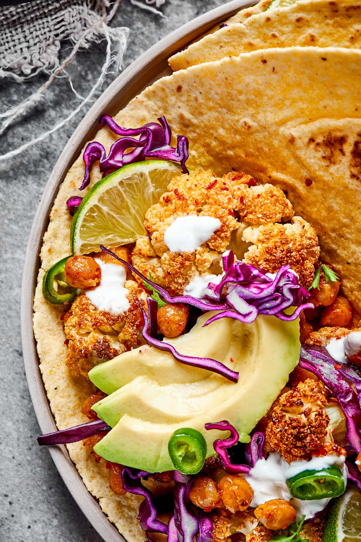 These roasted cauliflower and chickpea tacos are spicy, fresh, bursting with flavor, and a healthy vegetarian Mexican dinner Close up of half a roasted cauliflower and chickpea taco, topped with avocado, lime crema, and fresh jalapeños