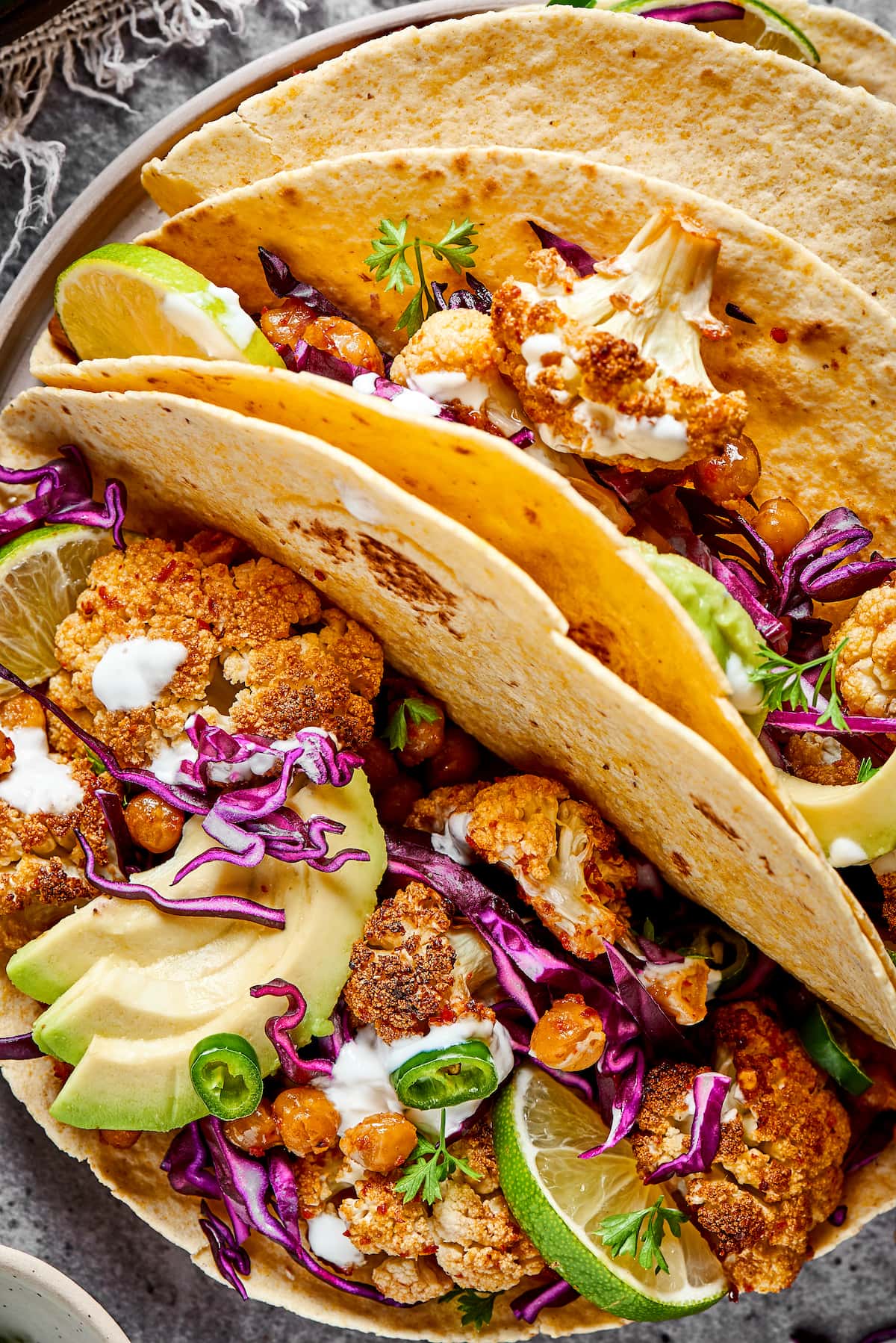 These roasted cauliflower and chickpea tacos are spicy, fresh, bursting with flavor, and a healthy vegetarian Mexican dinner Close up of three roasted cauliflower and chickpea tacos on a plate