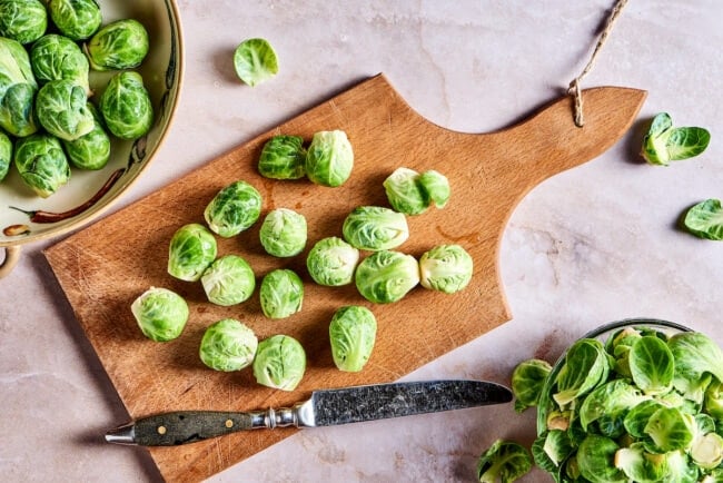 This roasted brussels sprouts recipe uses balsamic vinegar for an easy and flavorful Italian side dish that's healthy and vegetarian. Raw Brussels sprouts on a cutting board, with a knife on the cutting board, next to a bowl of Brussels sprouts and a bowl of the outer layers.