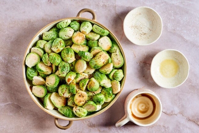 This roasted brussels sprouts recipe uses balsamic vinegar for an easy and flavorful Italian side dish that's healthy and vegetarian. A mixing bowl full of Brussels sprouts, coated in salt, pepper, olive oil, and balsamic vinegar, next to three small empty bowls