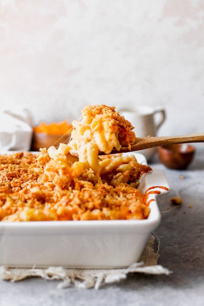This Family Favorite Baked Mac And Cheese Is Creamy, Cheesy, And Finished With A Buttery Panko Cracker Topping. Serve As A Main Dish Or Side Dish, It Is The BEST Homemade Mac And Cheese Recipe! #macandcheese #bakedmacandcheese #macaroniandcheese #pasta #easyrecipe #kidfriendly #dinner #vegetarian #macaroni a wooden spoon scooping mac and cheese out of a baking dish.