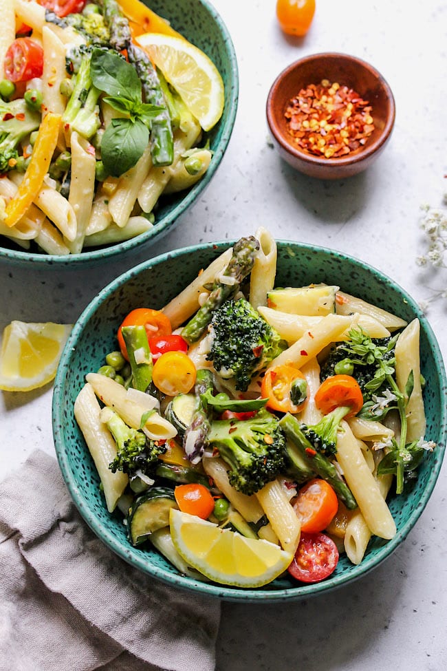 Pasta Primavera in bowls with fresh herbs and crushed red pepper flakes.