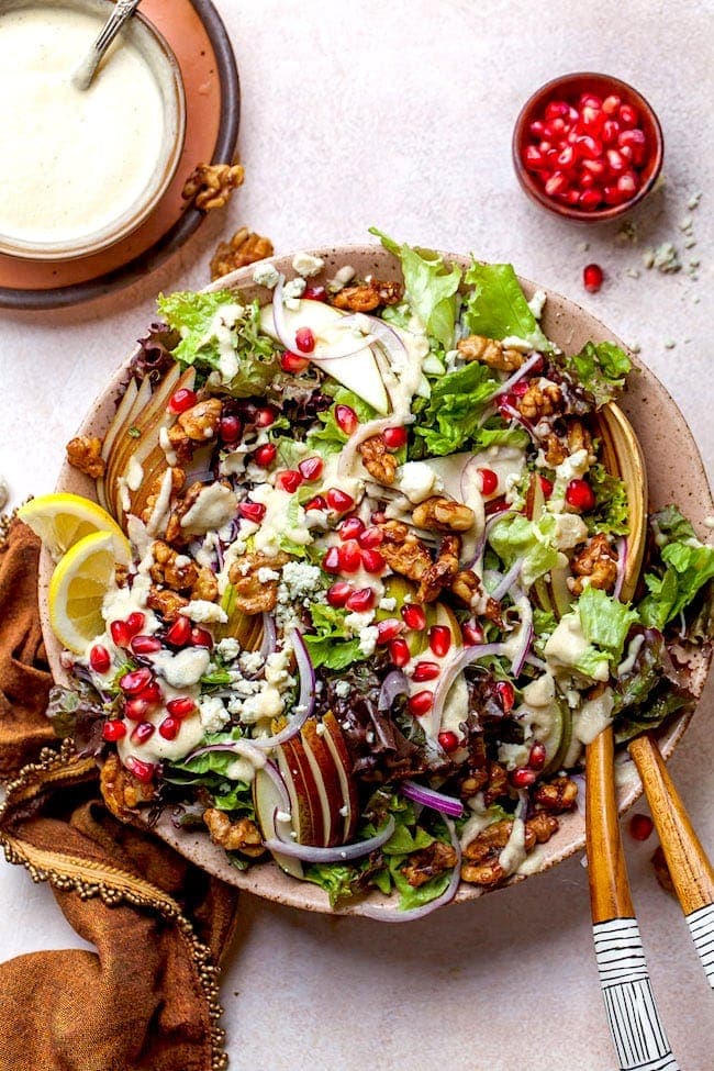 Pear Salad with candied walnuts and pomegranate in serving bowl with salad servers. 