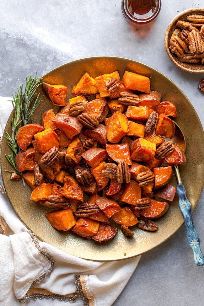 Maple Roasted Sweet Potatoes on plate with spoon and pecans and rosemary. 