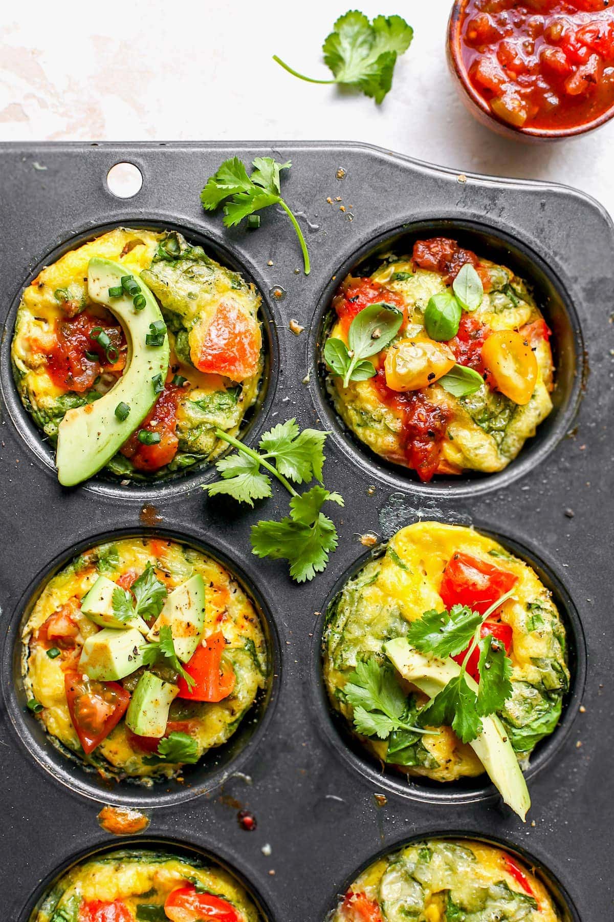 Egg Muffins in muffin tin with avocado and herbs.
