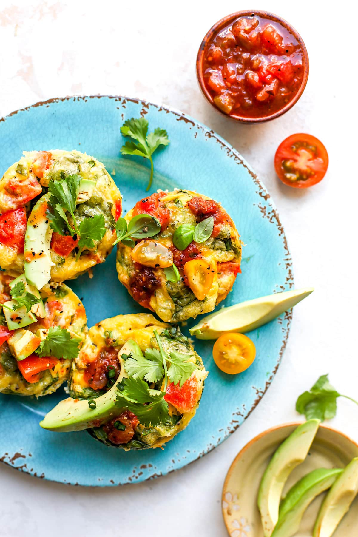 Egg muffins on plate with avocado, herbs, and salsa.