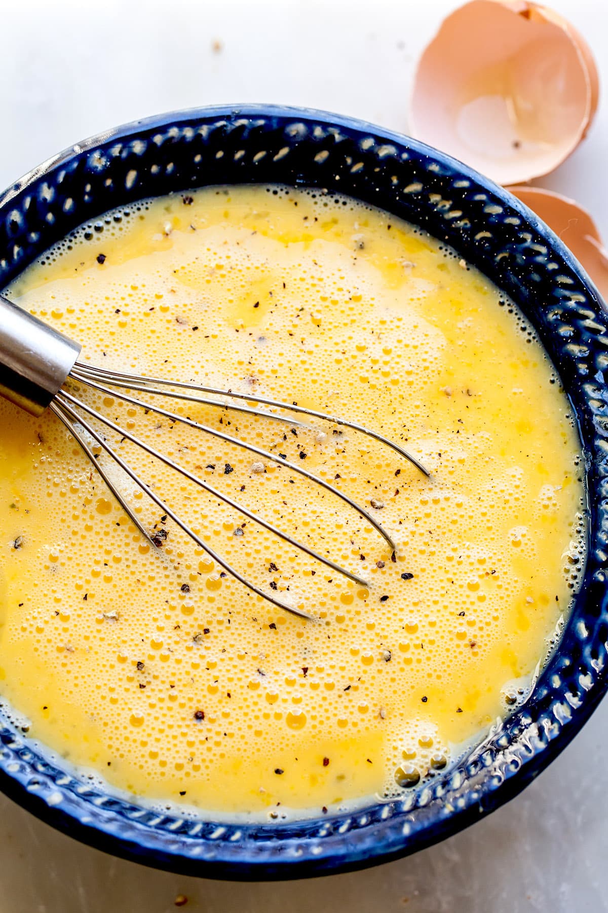 eggs being scrambled in a bowl with a whisk to make egg muffins.