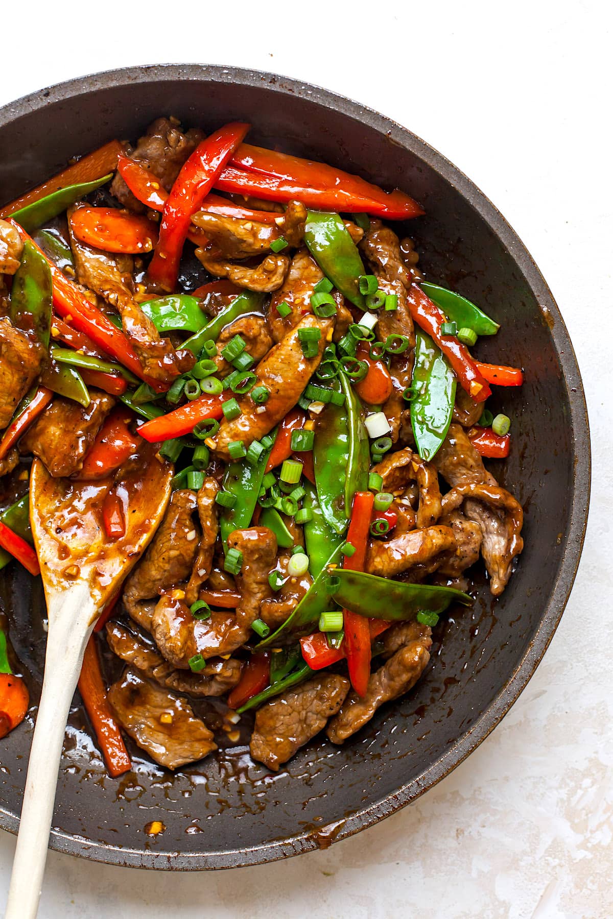 Beef stir fry with vegetables in skillet with wooden spoon.