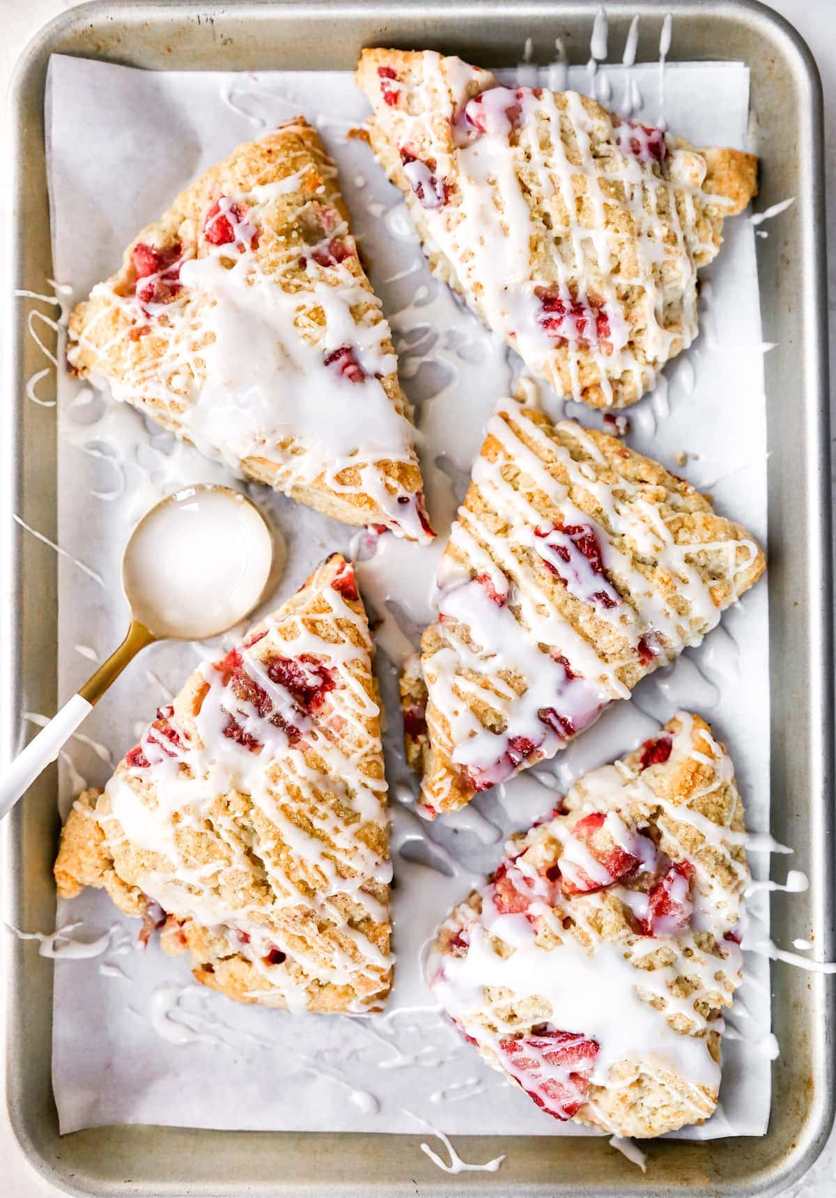 Strawberry Scones with glaze on baking sheet with parchment paper.