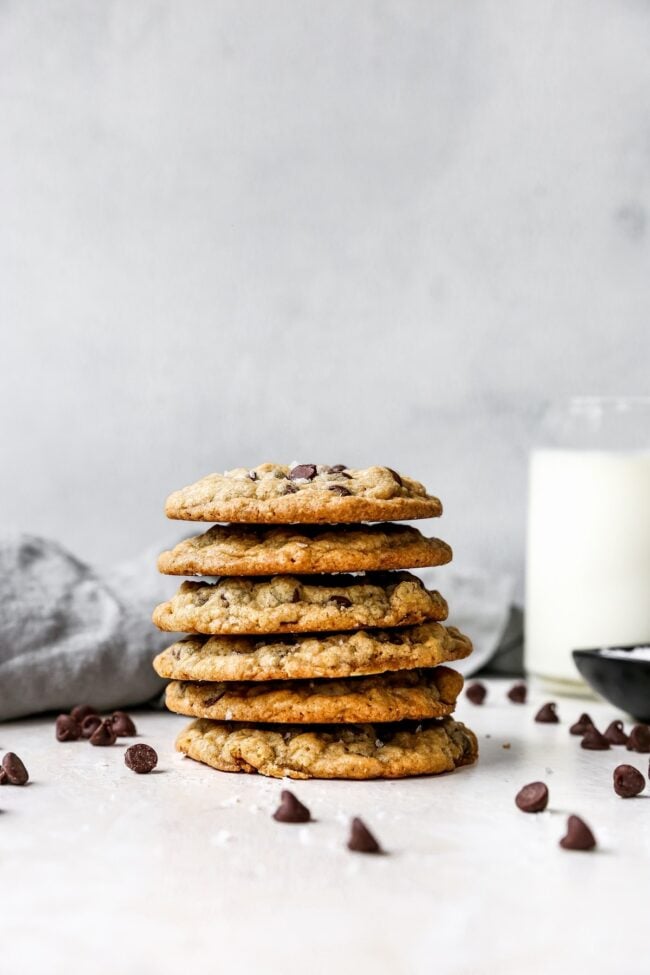 Stack of Doubletree Cookies with glass of milk and chocolate chips.