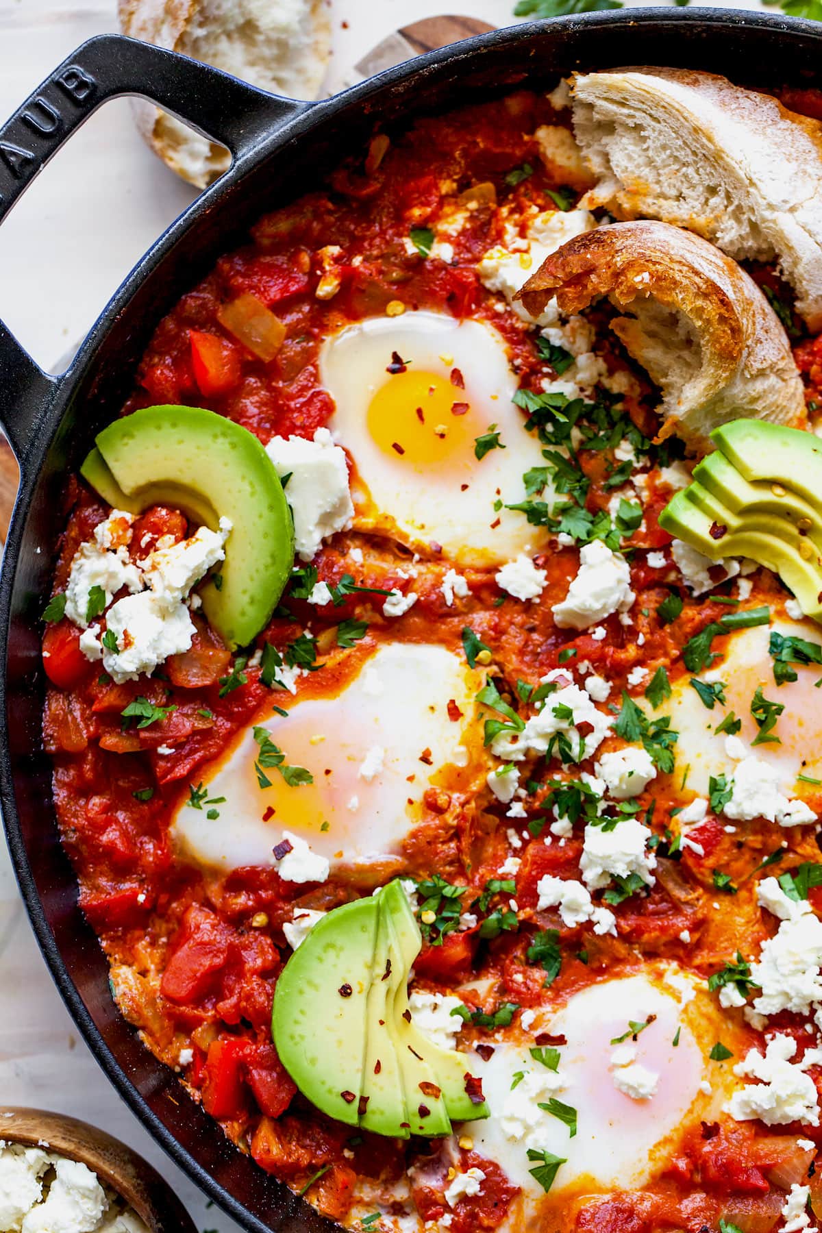 Shakshuka Eggs in skillet with feta cheese, herbs, and avocado slices.