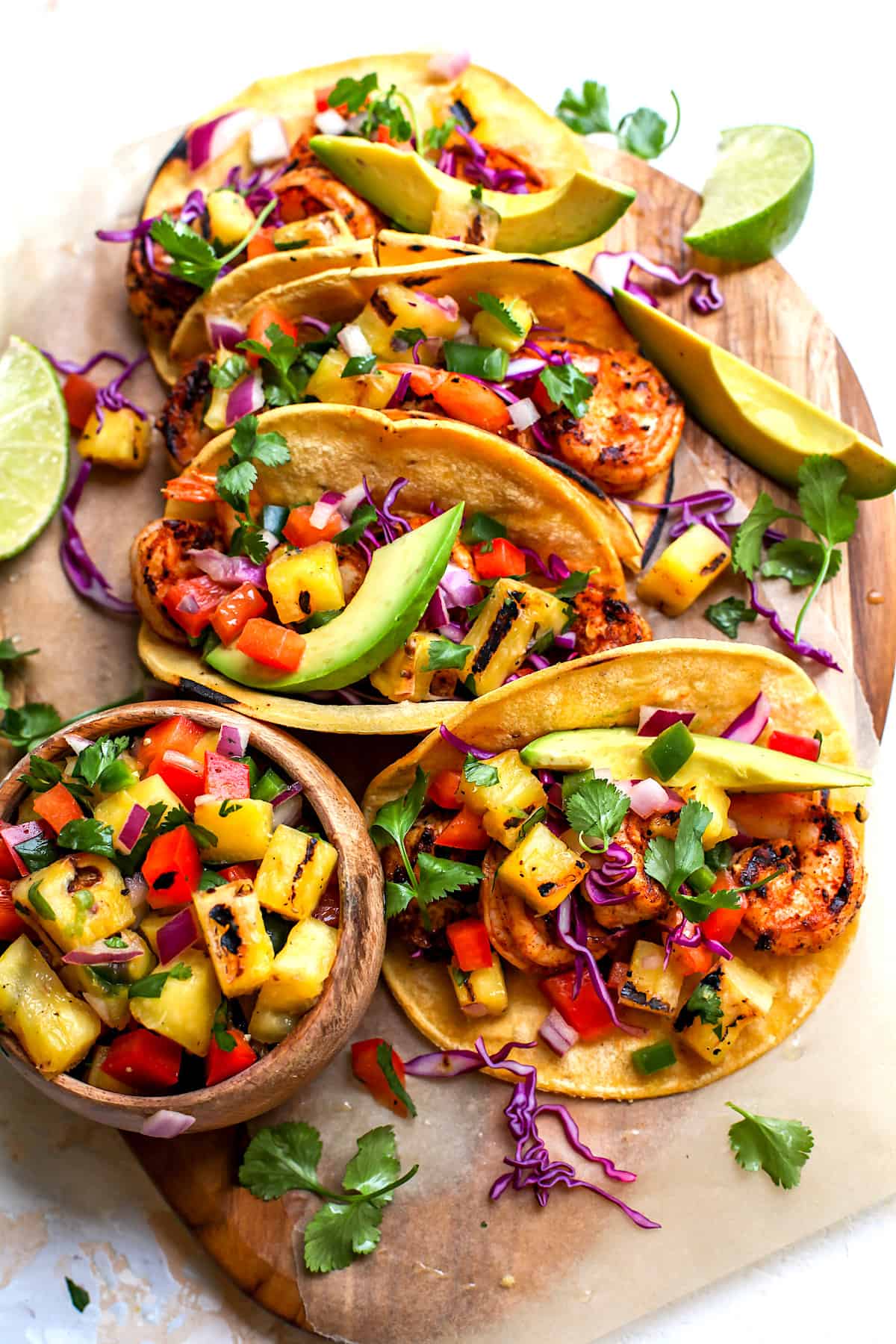 shrimp tacos in corn tortillas with grilled pineapple salsa, avocado, and cilantro on wood board.