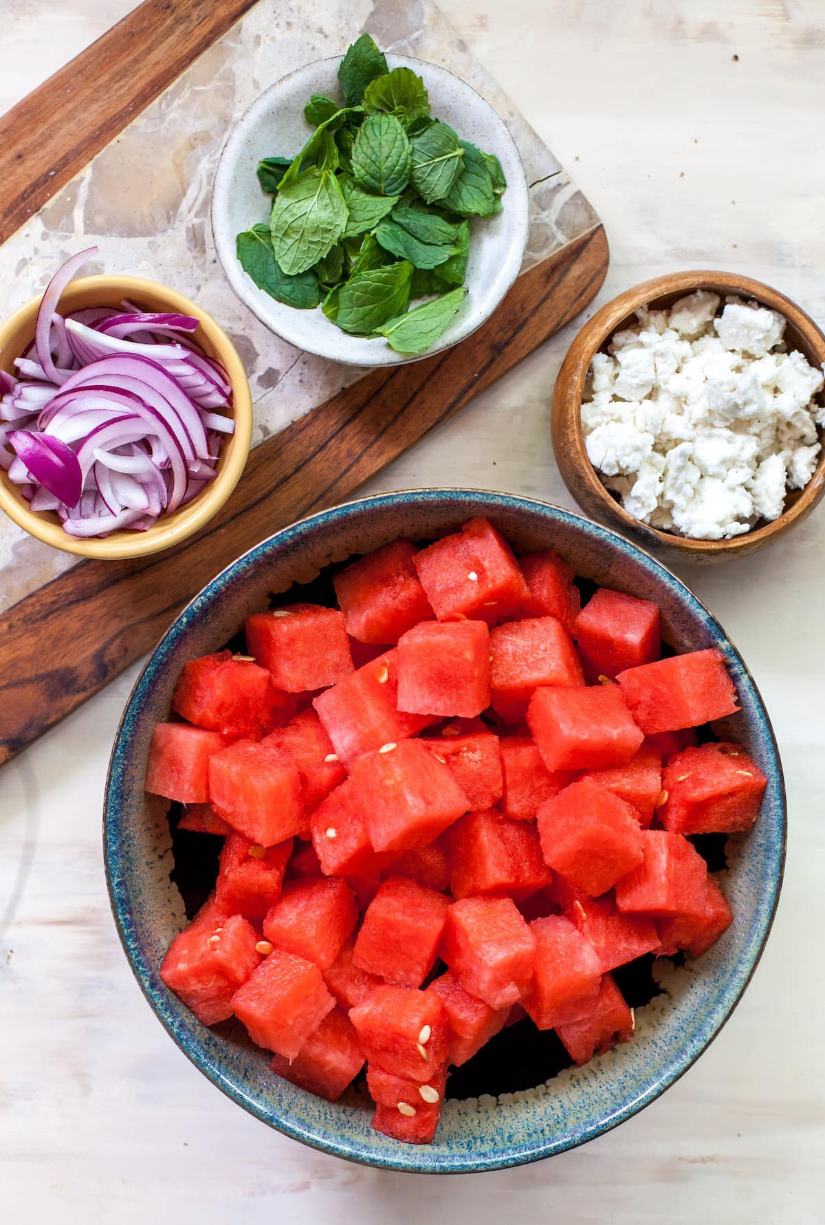 Watermelon, feta, red onion, and mint in bowls to make watermelon feta salad.