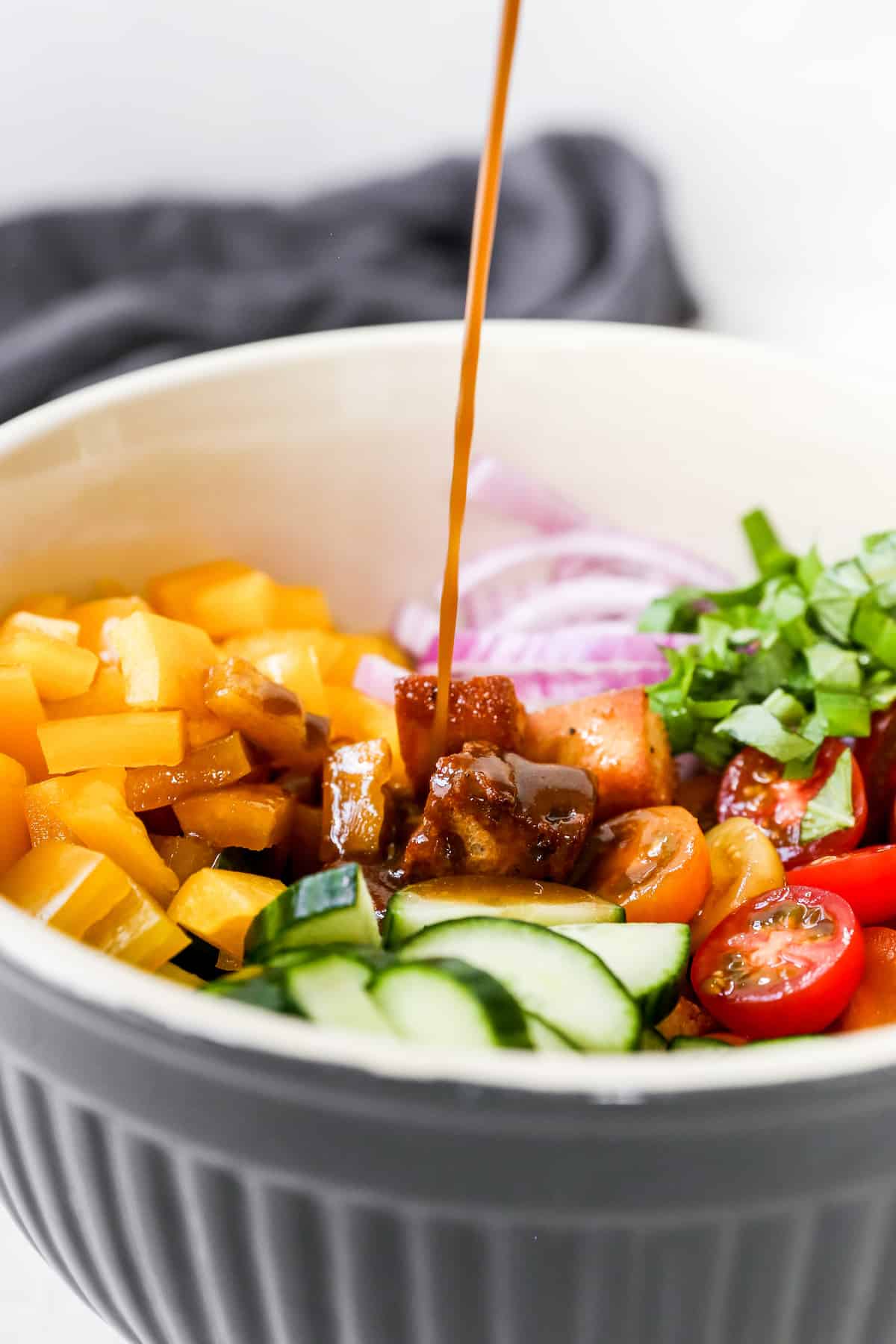 Balsamic vinaigrette pouring over Panzanella in white serving bowl.