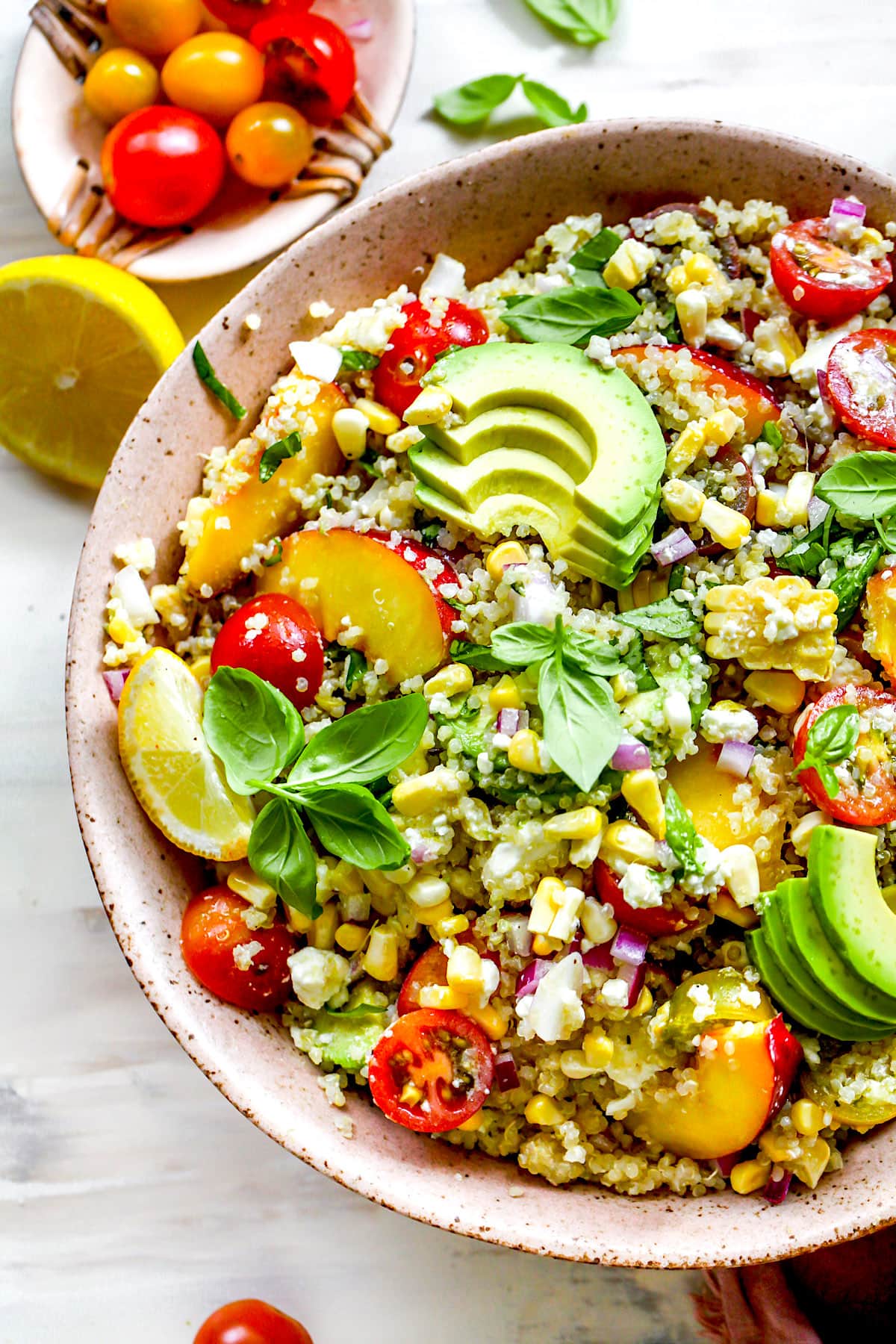 summer quinoa salad in bowl with avocado slices, lemon, and fresh basil.