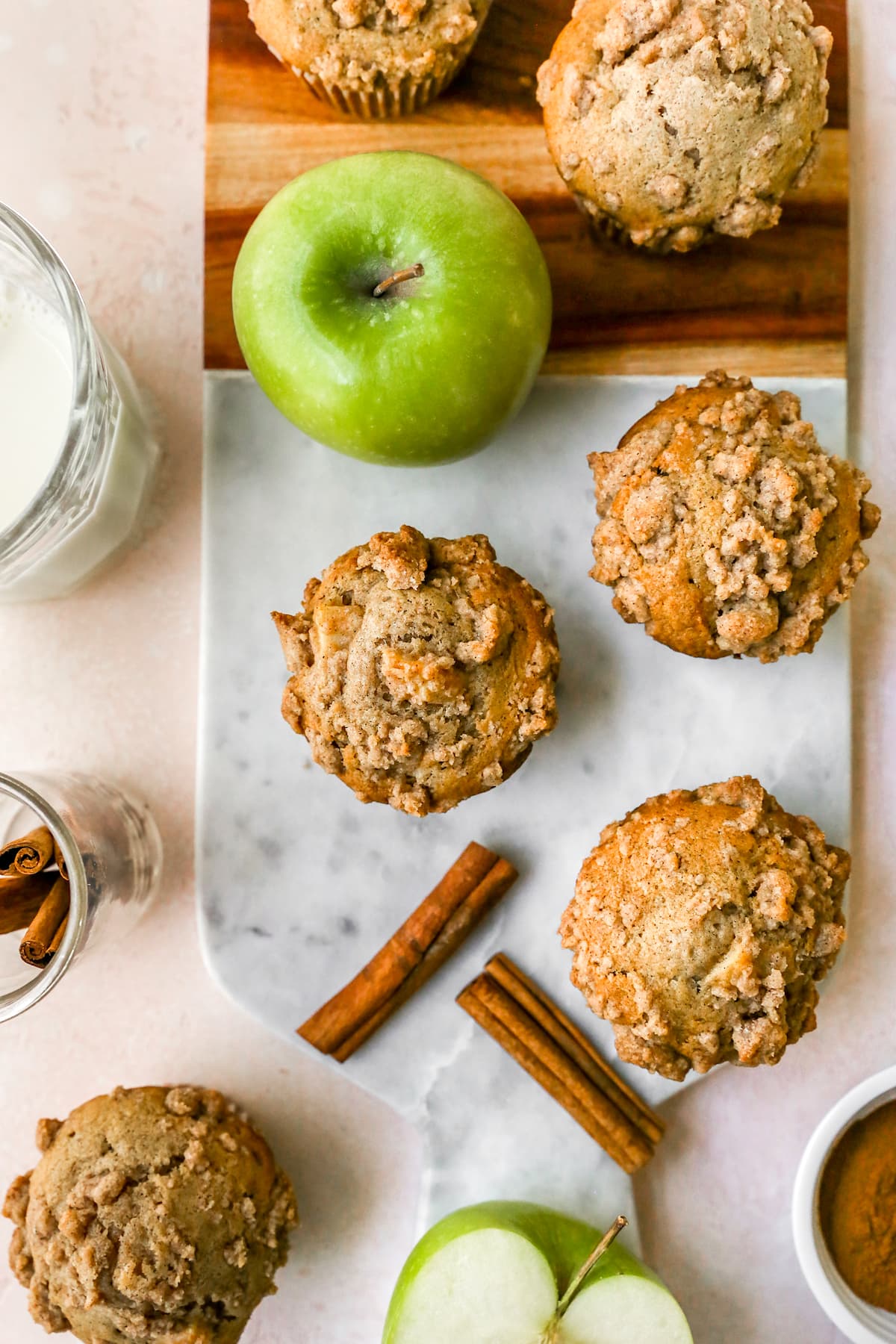 Apple Cinnamon Muffins with crumb topping on board with apples and cinnamon sticks.