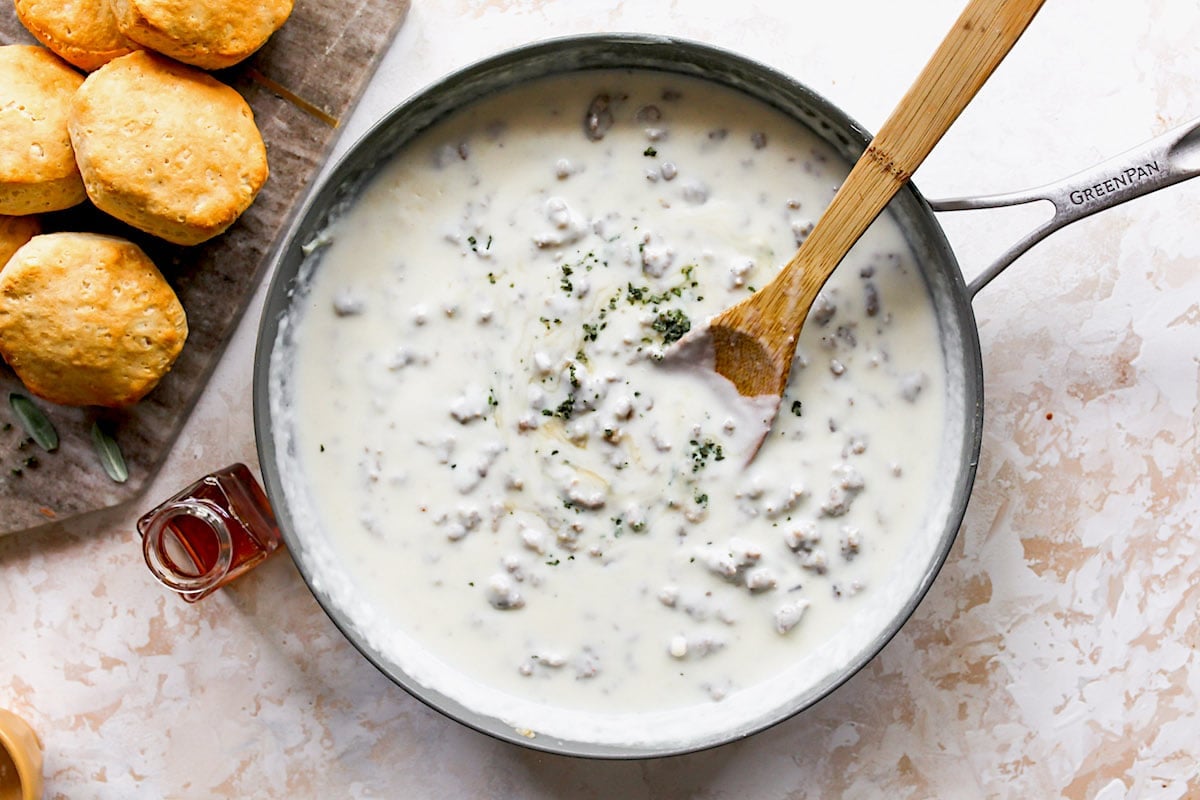 sausage gravy in skillet with wooden spoon to make biscuits and gravy.