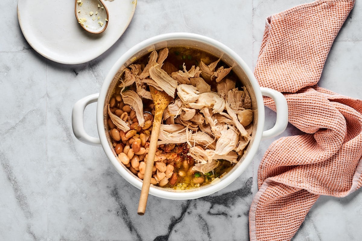 This comforting white chicken chili is easy to make with white beans, zesty seasonings, and rotisserie chicken. A favorite weeknight meal! Shredded chicken and white beans added into a large pot with sautéed garlic, onions, and jalapeños.