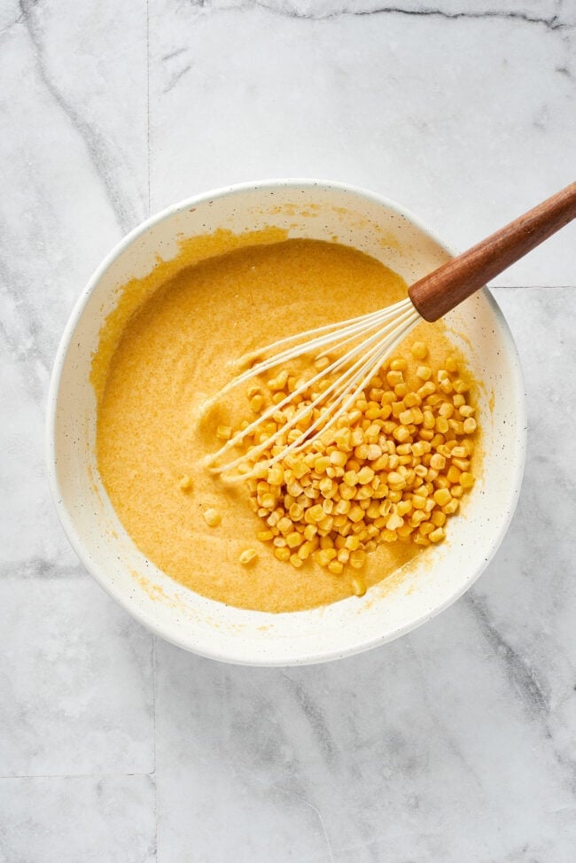 This easy cornbread recipe is tender, moist, perfectly sweet, and takes only 35 minutes to make, making it a wonderful side dish A mixing bowl with cornbread batter, with corn kernels on top, and a whisk