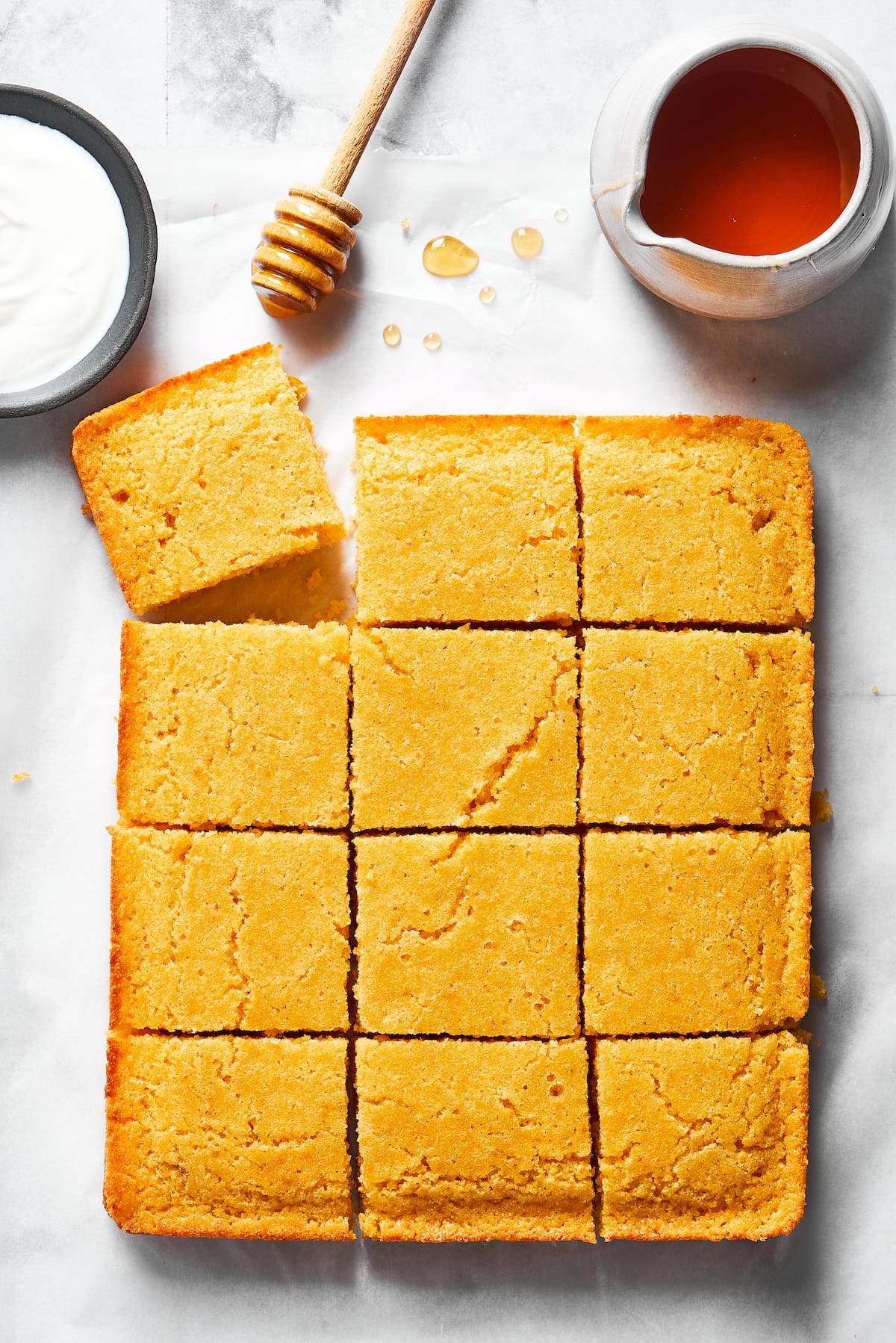 This easy cornbread recipe is tender, moist, perfectly sweet, and takes only 35 minutes to make, making it a wonderful side dish Cornbread cut into 12 pieces, with one corner askew, next to a jar of honey and a honey stirrer