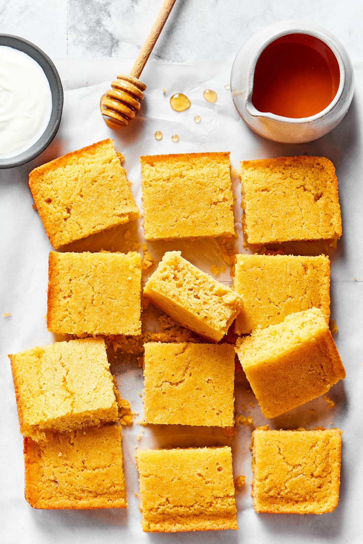 This easy cornbread recipe is tender, moist, perfectly sweet, and takes only 35 minutes to make, making it a wonderful side dish Slices of cornbread on a counter, next to a bowl of honey, a honey stirrer, and a bowl of creme fraiche