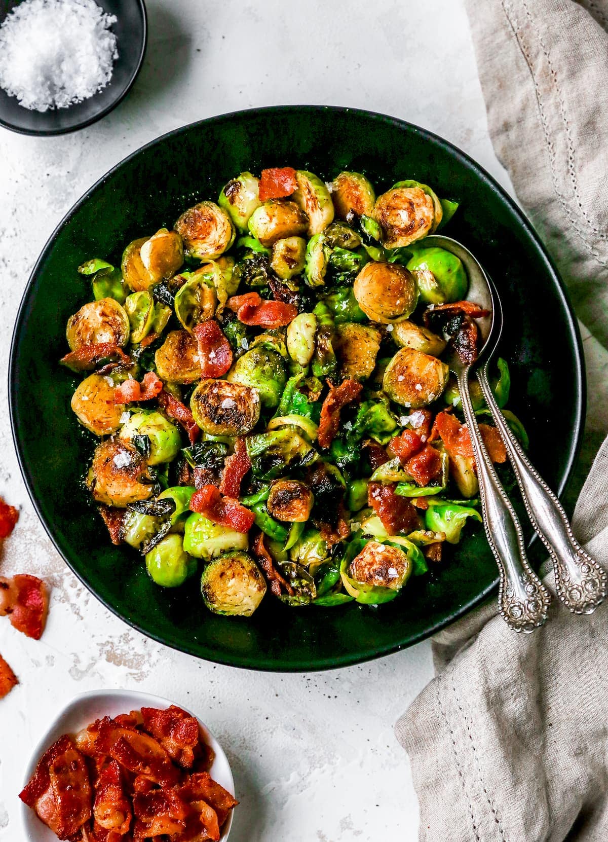brussels sprouts with bacon in black bowl with serving spoons.