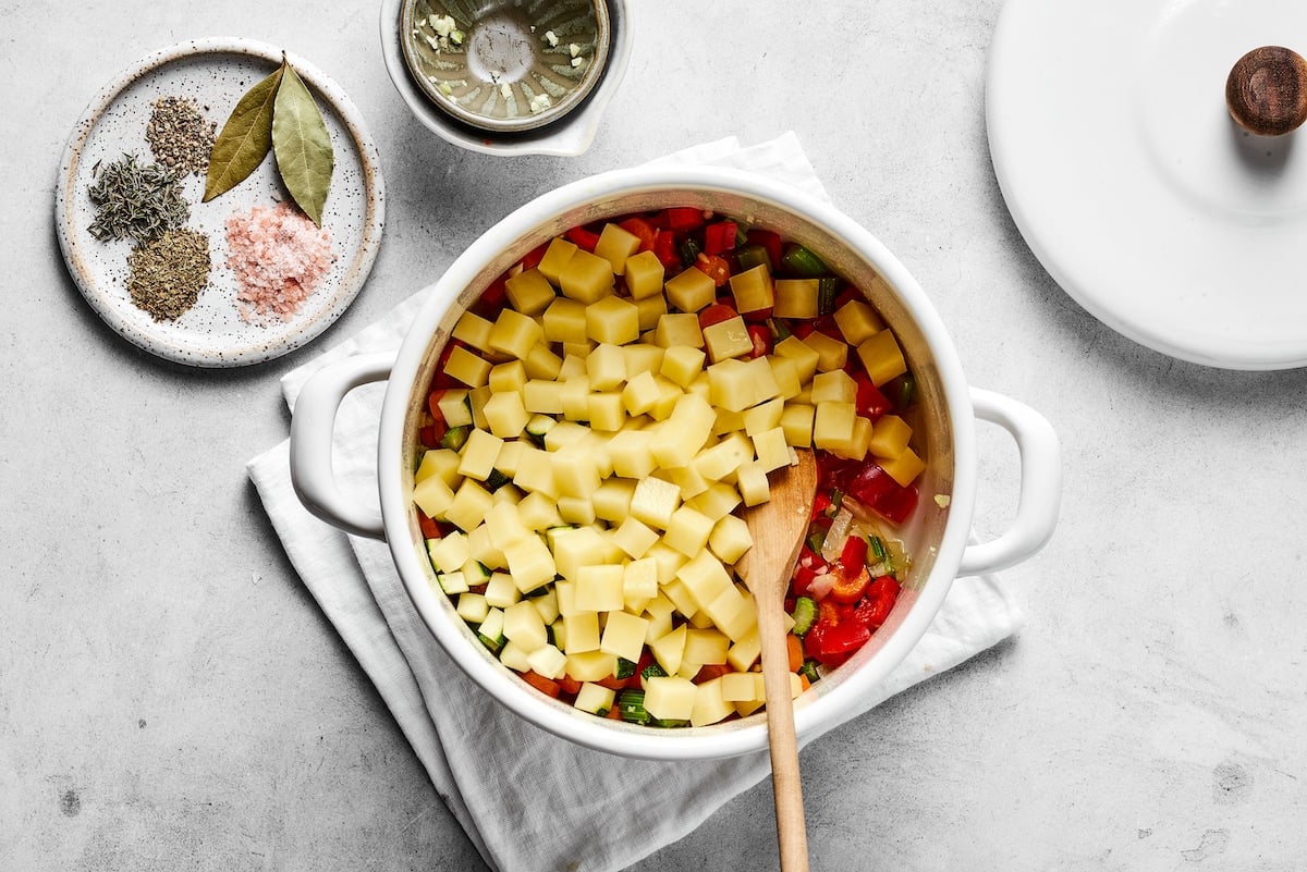 This comforting homemade vegetable soup recipe is a family favorite that's so much better than canned soup! Enjoy a bowl for lunch or dinner. Chopped potatoes are added into the sautéed veggies in a saucepan.