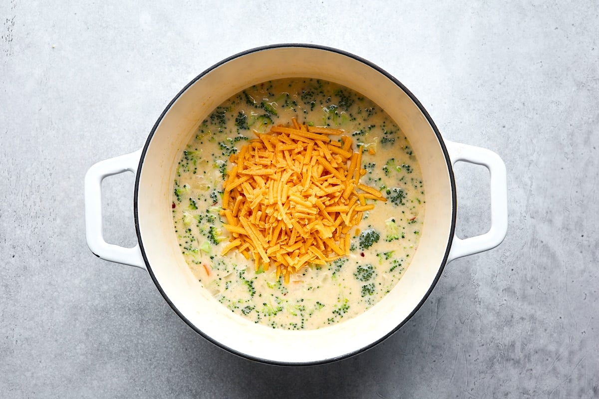 shredded cheese being added to broccoli cheese soup in pot.