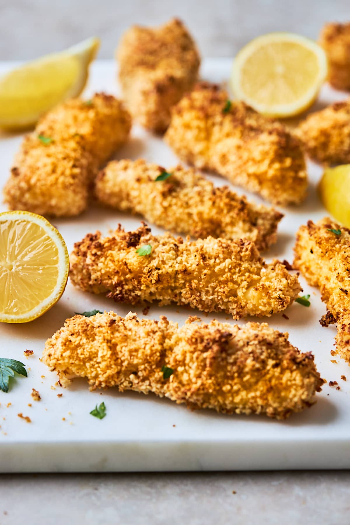 homemade crispy fish sticks with lemons on white board.