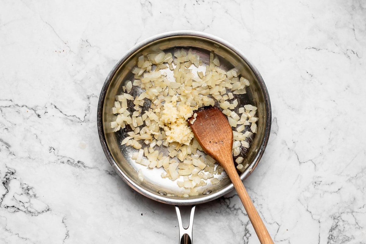 onions sautéing in skillet with wooden spoon.